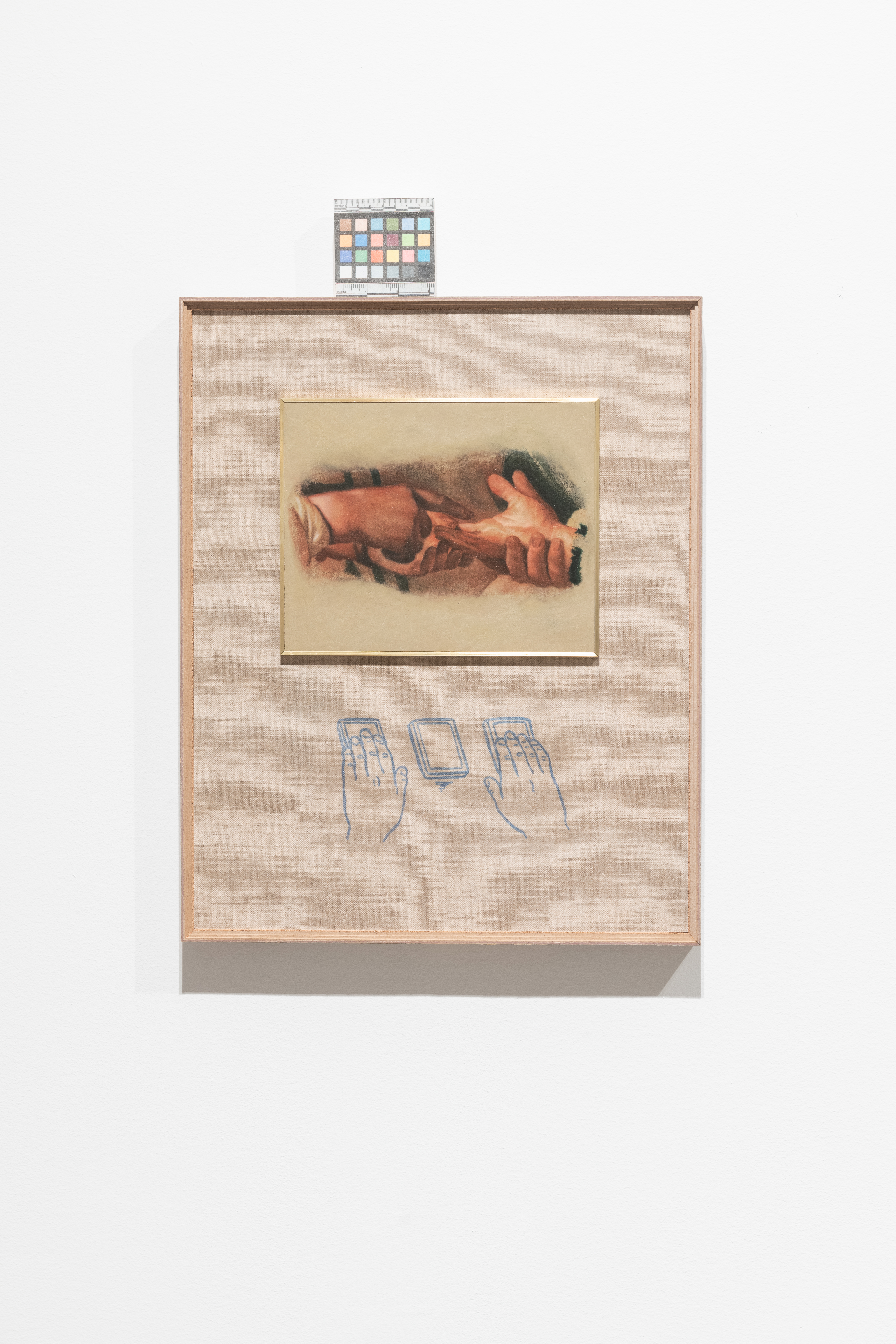 A color photograph of a framed painting of two sets of hands. On top of the frame rests a color control strip.