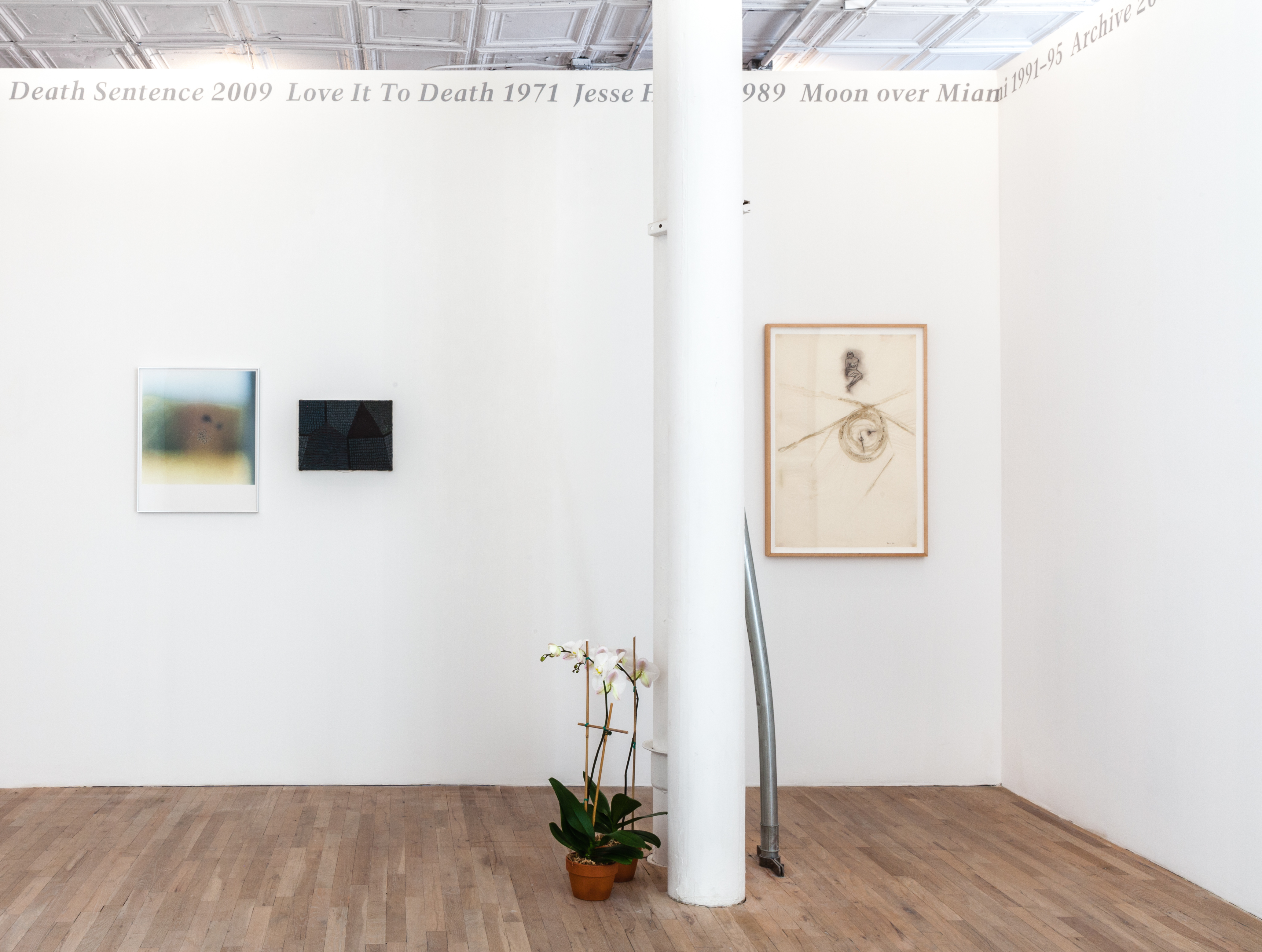 Silver, italic text displayed across the top edges of two adjacent white, gallery walls reads, 