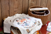 A white, graphic shirt sits on a piles of items next to nested wicker baskets in front of a wooden wall. On top of the baskets is a sign that reads, 