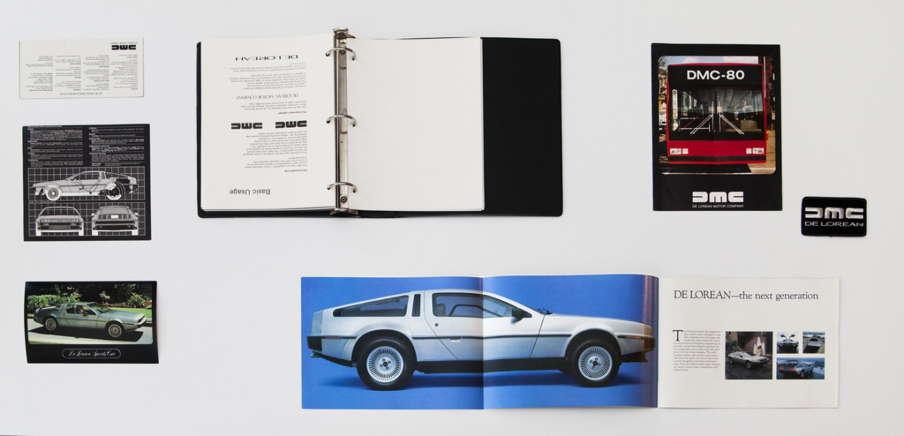 Assorted Delorean paraphernalia displayed on a white background, including several images of cars and a binder filled with a user manual.