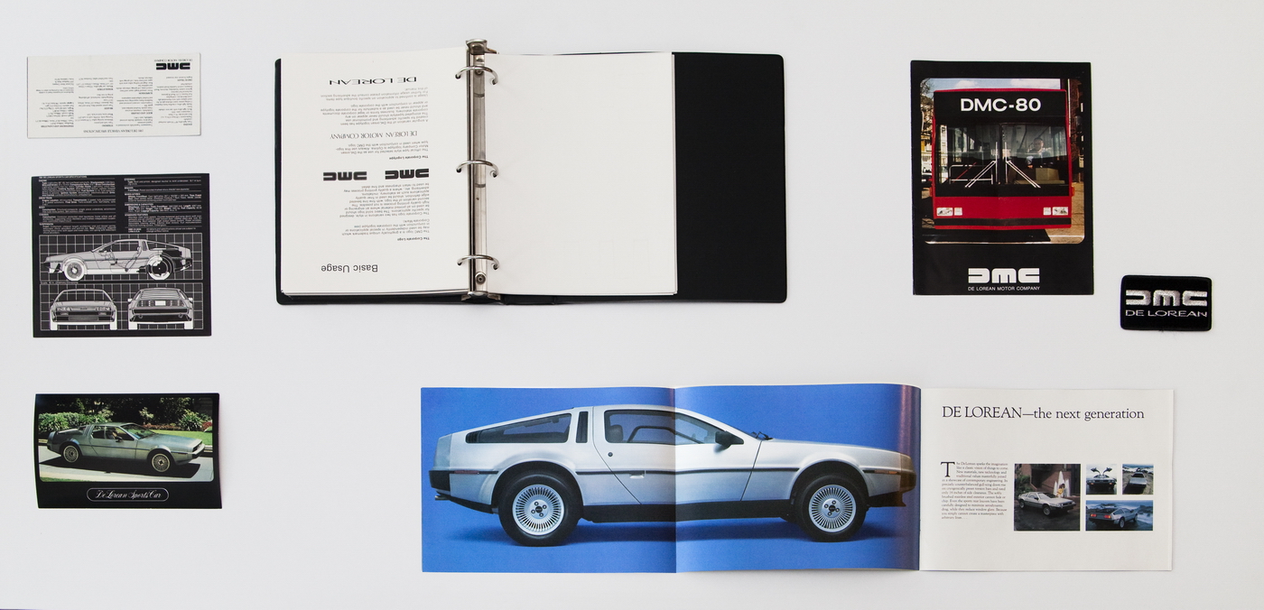 Assorted Delorean paraphernalia displayed on a white background, including several images of cars and a binder filled with a user manual.
