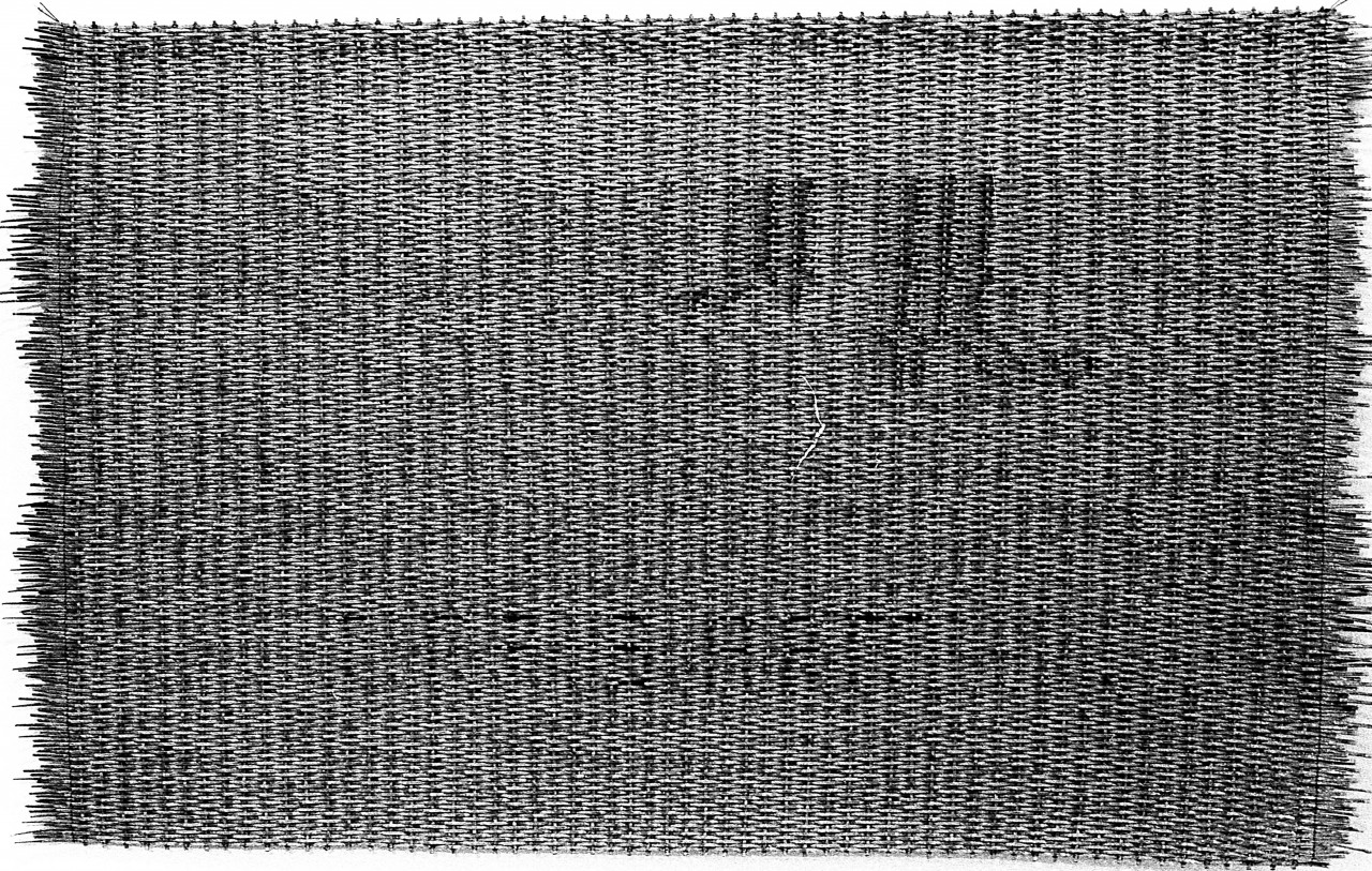 A black and white photograph of a woven mat on a white background.