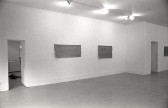 A black and white photograph of a gallery space, three mats are visible hanging on the wall.