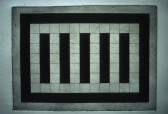 A painting with 5 black vertical rectangles in the center srrounded by indvidually outlined white squares inside a larger black rectangular outline on a white canvas hanging on a white wall.
