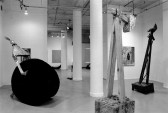 Three abstract sculptures in the foreground of a white-walled gallery space with white columns.  In the background, there are other gallery spaces with artworks hanging on the walls.