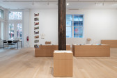 A large gallery space houses a variety of plinths made of MDF atop of which are placed various archival documents and objects, such as exhibition pamphlets and art historical journals. 