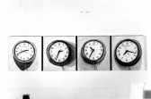 A black and white photgraph of four square paintings of clocks in a horizontal line, each showing a different time.
