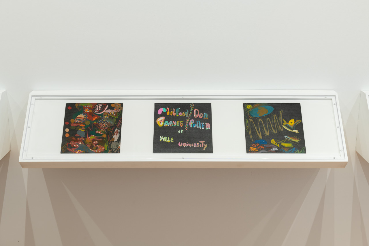 A color photograph of three handpainted LPs in a wall mounted vitrine.