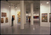 A photograph of a white walled gallery space densely hung with figurative paintings.