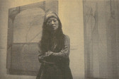 Faded photograph of artist Miyoko Ito standing with her arms crossed in front of two of her paintings.
