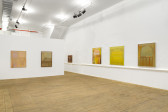 Six paintings are hung on white walls at eye level. The paintings contain muted and vibrant warm colors depicting abstract shapes.