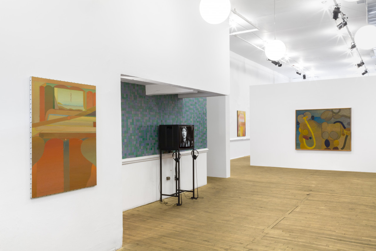 In the foreground, a painting hung on a white wall features warm hues. A television monitor is installed in an alcove, and a woman