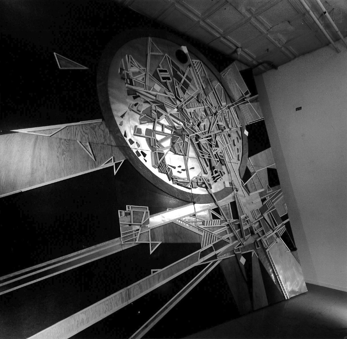 A composition of lines, circles, and angles made of wood and metal is affixed to a wall, covering the surface.