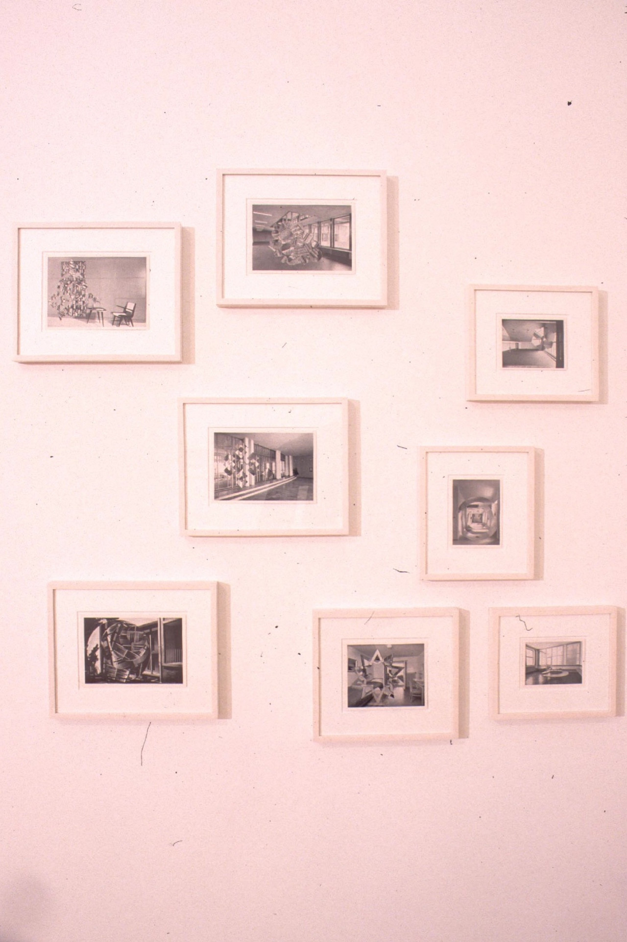 A series of small, black and white photo-collages displayed in white frames on a gallery wall. The collages depict various interior spaces overlaid with geometric cut-outs of other photographic images.