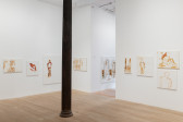 A series of paintings are hung along four gallery walls. Many of the paintings loosely depict human figures or abstracted body parts in brown and red toned paint against white backgrounds.
