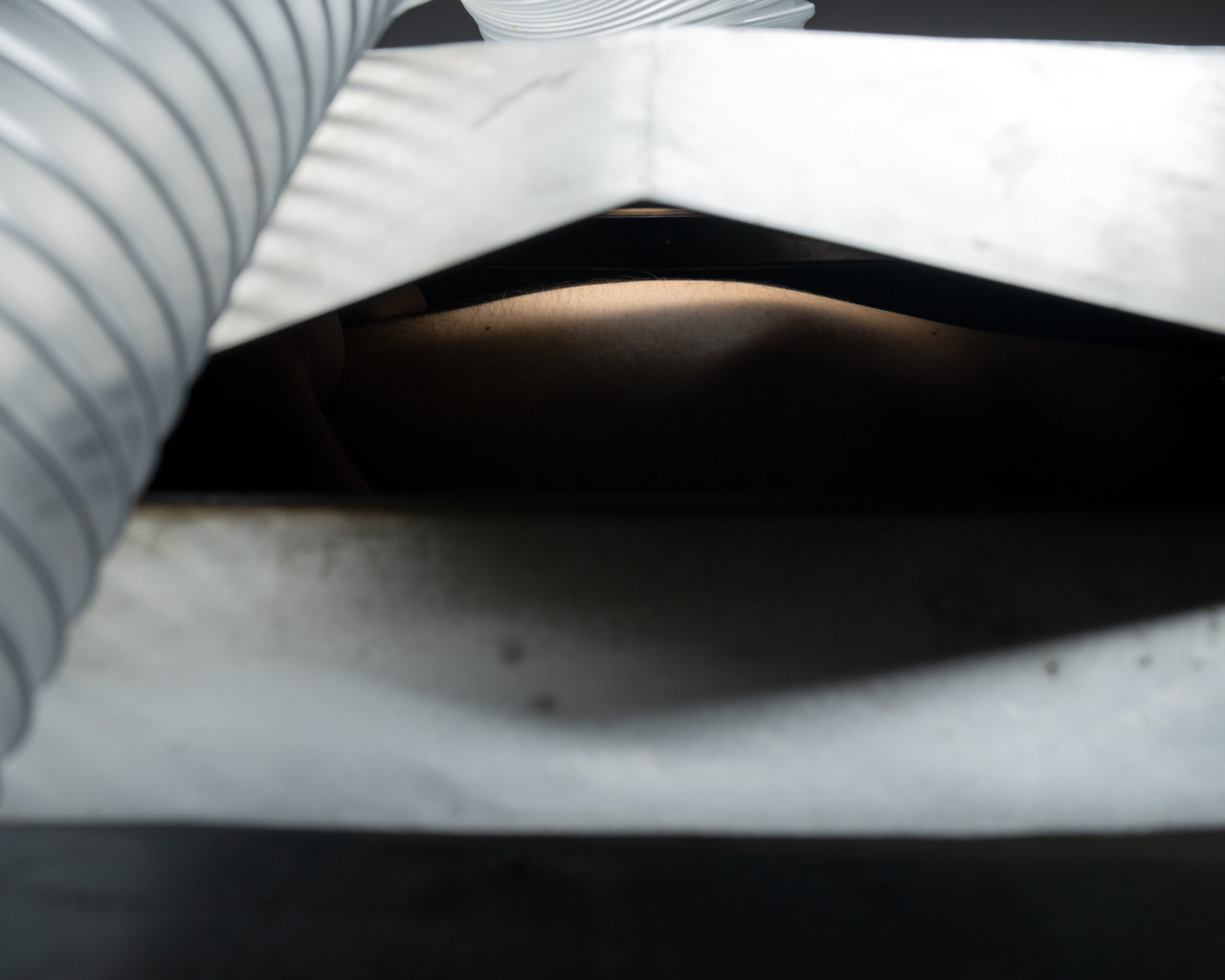 In this close-up shot, a white pleated structure resembles a tent structure. Underneath the pleat there appears a backlit illumination. In the left side of the frame a ventilation tube extends from the front towards the back of the white structure.