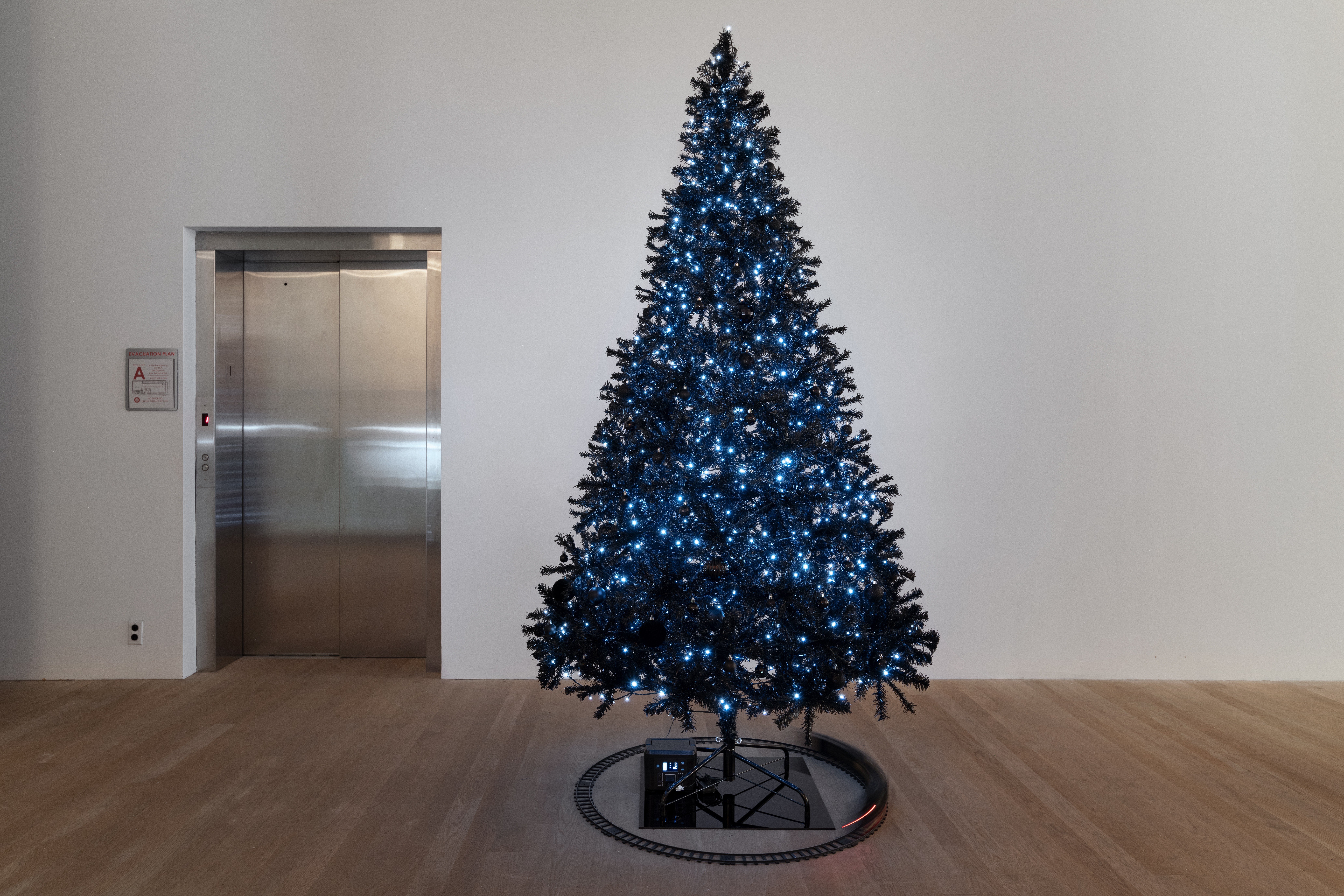 A black Christmas tree stands in the room, adorned with white twinkling lights. A black toy train circulates around the shiny black base of the tree. 