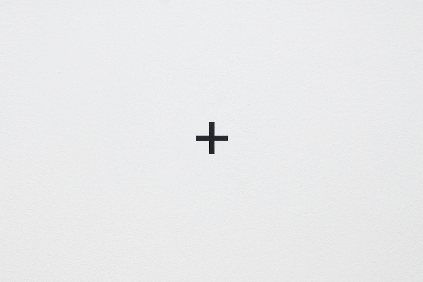 On a white gallery wall, a vinyl cut out of a black cross or 