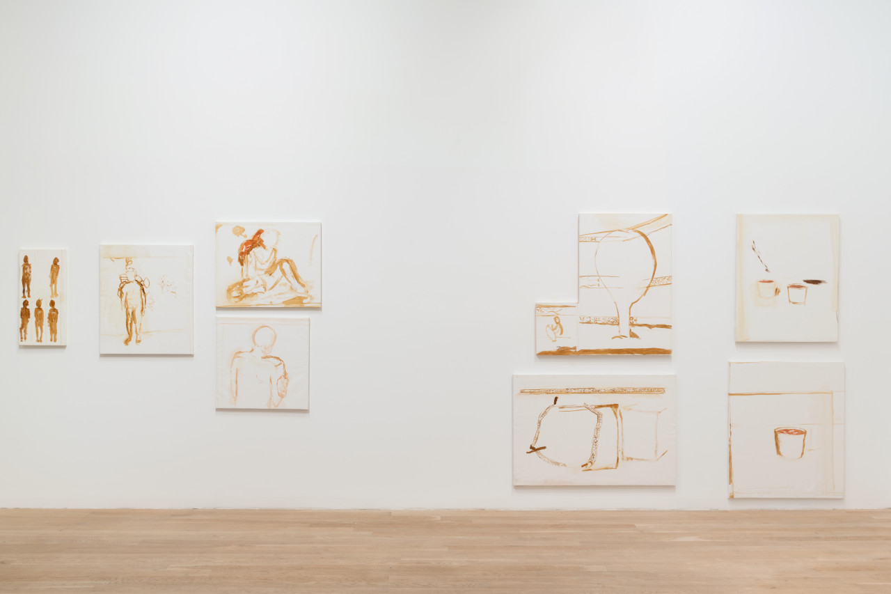 A series of paintings made with brown and red paint against a white background are hung on a wall.