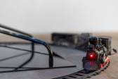 A red light beams from a black toy train as it moves along the train track. Smoke emits from the chimney of the toy train.