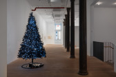 A twinkling black Christmas tree stands in the foreground as the gallery walls recede. A few paintings hang on the more distant walls. 