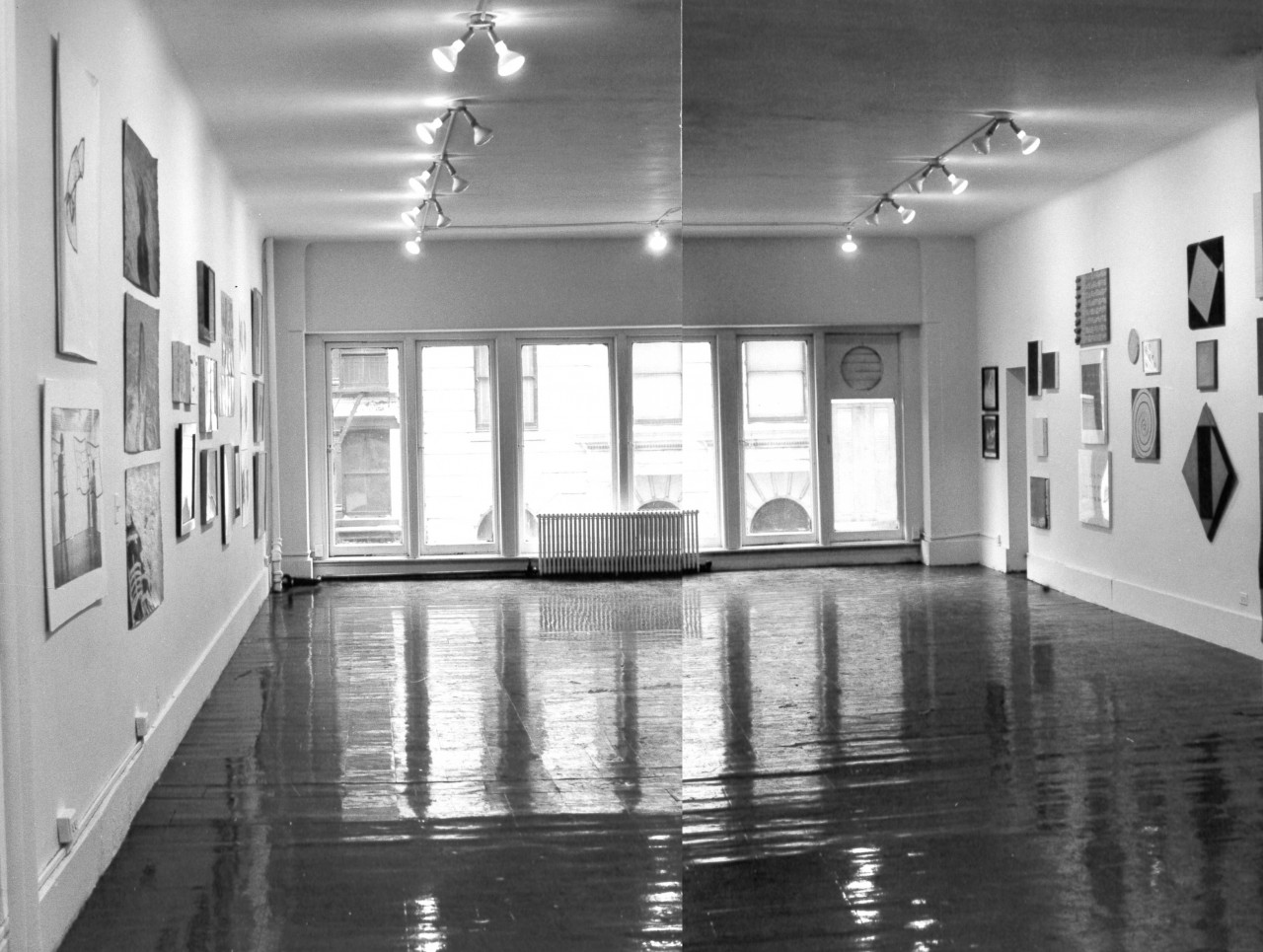 A black and white installation view of a gallery space with a set of six large window panes. Various pieces of artwork hang from the walls.