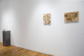 An installation view of two abstract wall works made of wood and a water fountain sculpture in the background.
