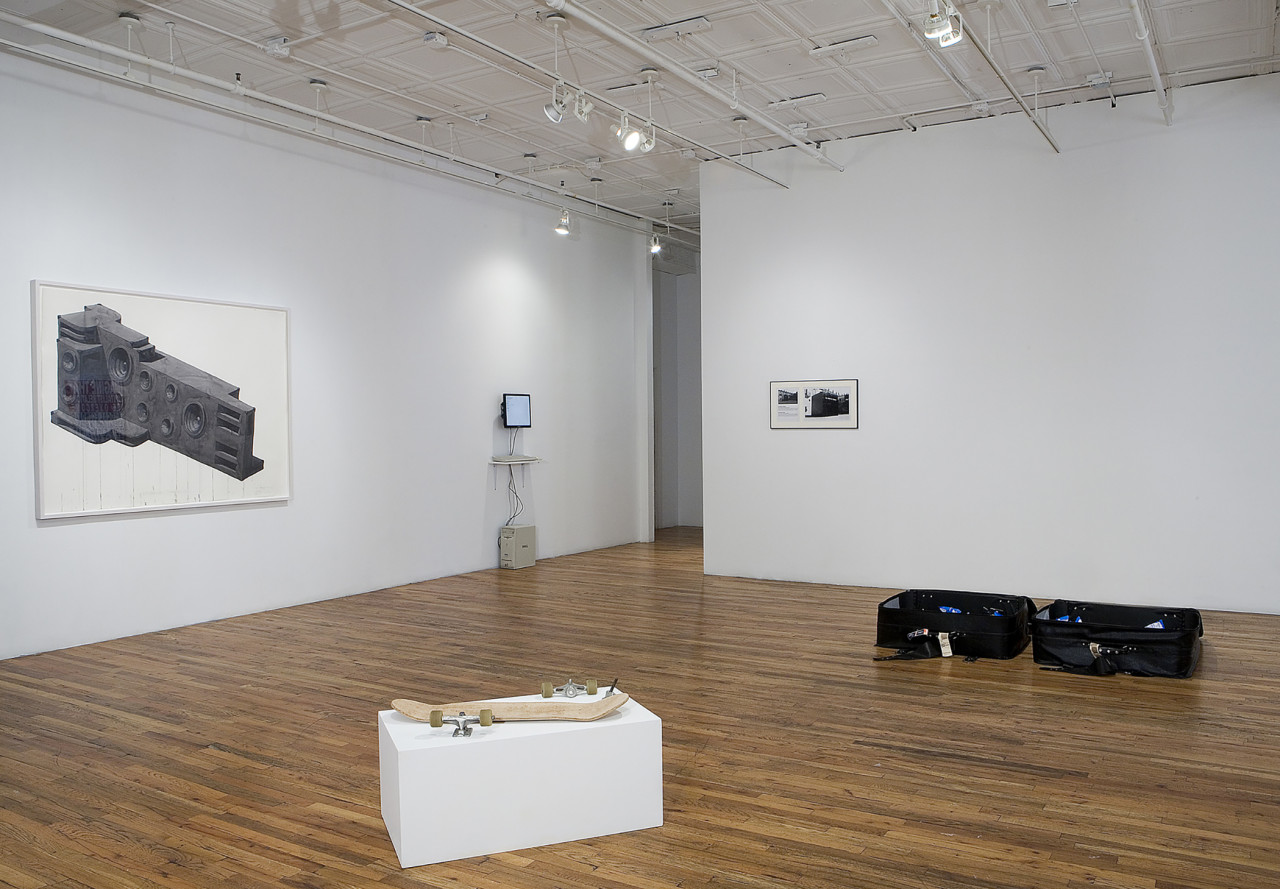 An installation view with a deconstructed skateboard on a pedestal in the foreground with two suitcases in the background and a two dimensional depiction of a stereo system along with other small wall works.
