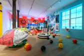 A wide angle image of a multicolored exhibition space consisting of beach paraphernalia.