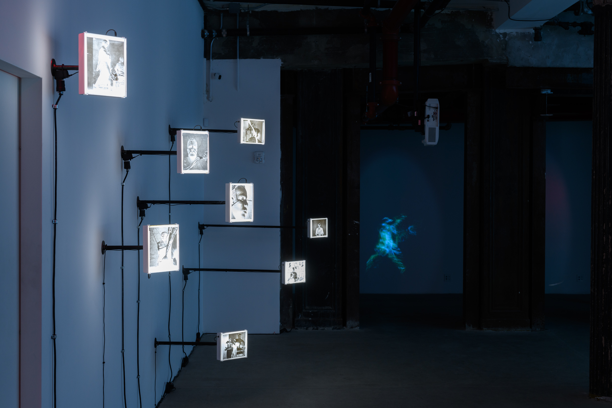 An image of a dark room with multiple videos playing in the background and photograph negatives hang off the wall.