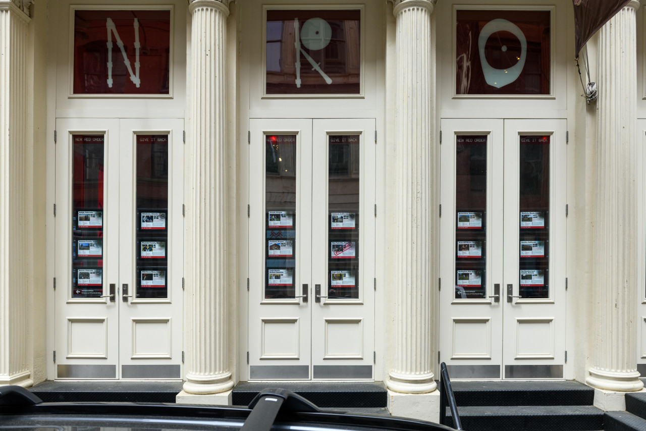 An image of a white facade with real estate listings in the windows, and above them, in vinyl lettering reads "NRO".