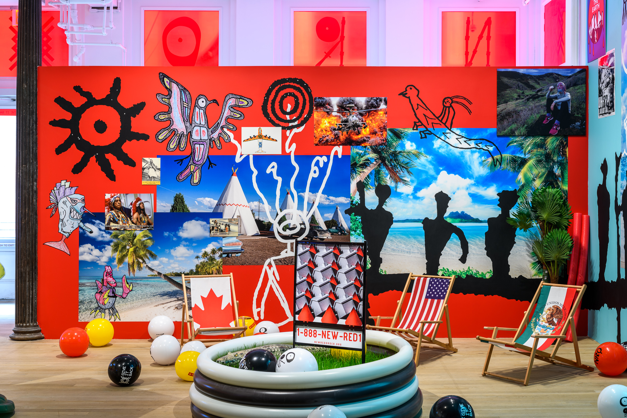 An image of a multicolored exhibition space consisting of beach paraphernalia, a real estate lawn sign, and a mural wall collaged with images and drawings.
