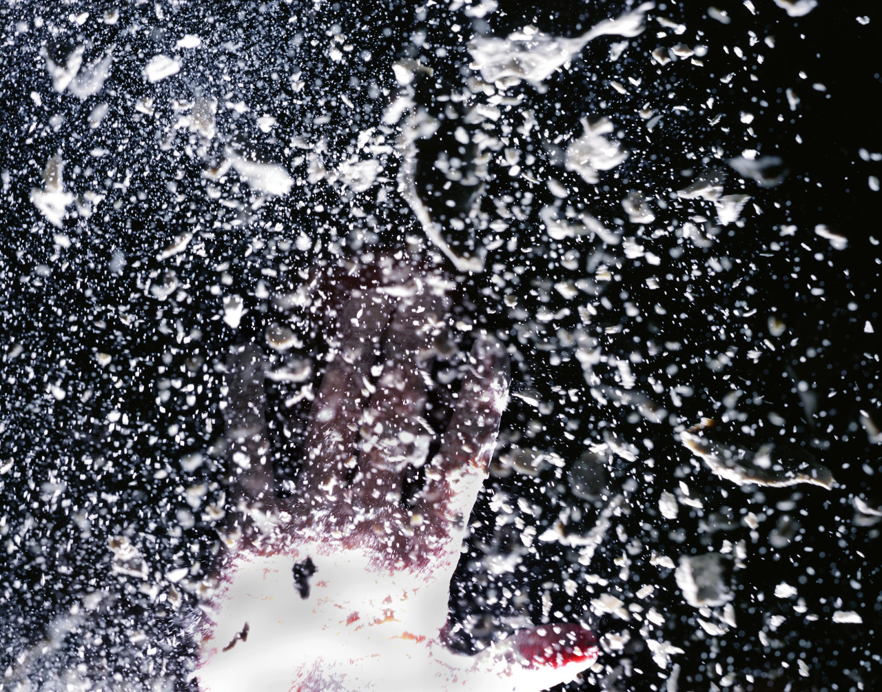 A hand extends its fingers admist a shower of droplets of liquid. A bright light shines on the hand and droplets.