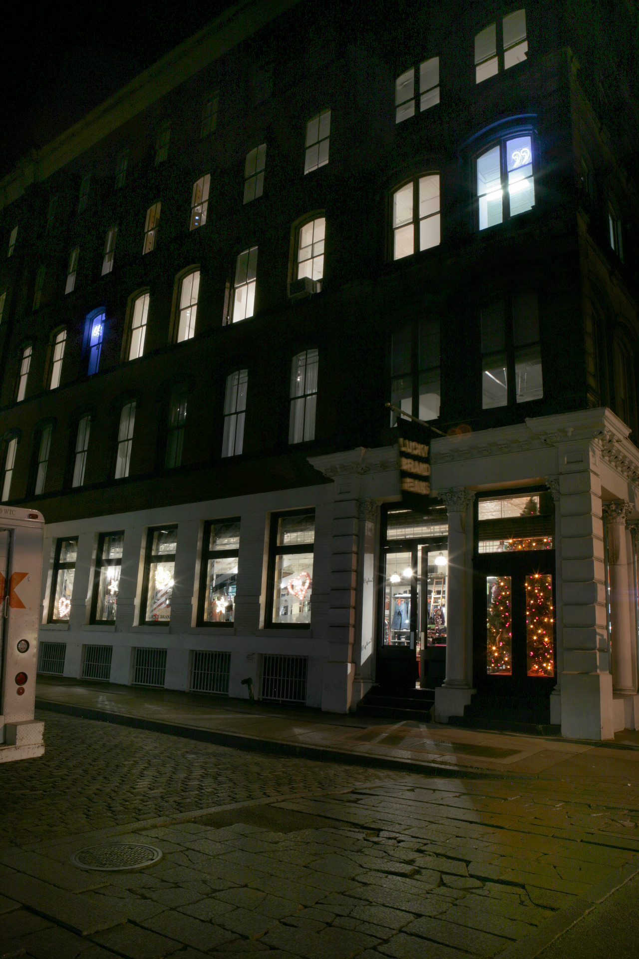 The exterior of a Soho building at night from the opposite street corner. Inside the third floor are two glowing blue neon quotation marks visible from outside.