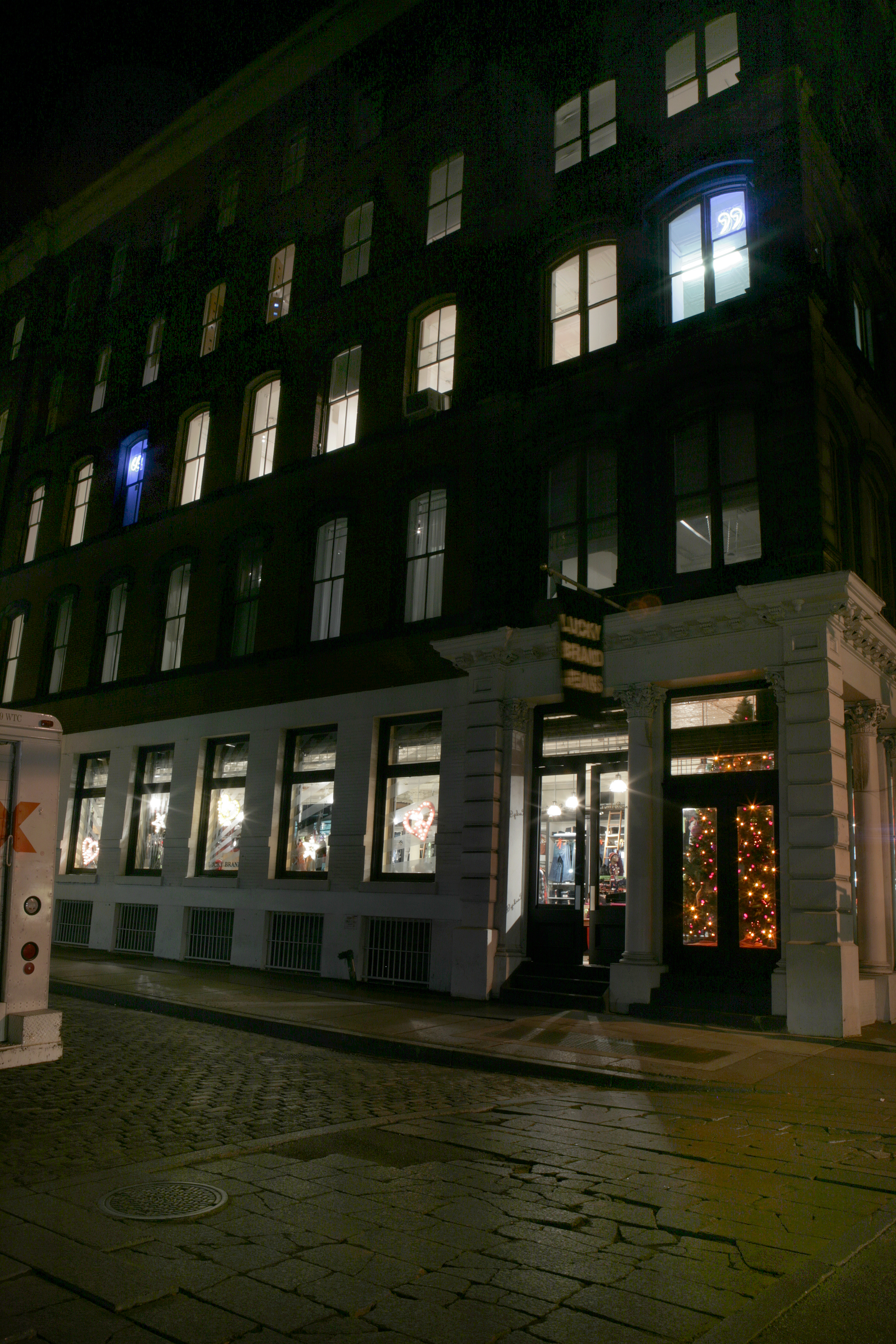 The exterior of a Soho building at night from the opposite street corner. Inside the third floor are two glowing blue neon quotation marks visible from outside.