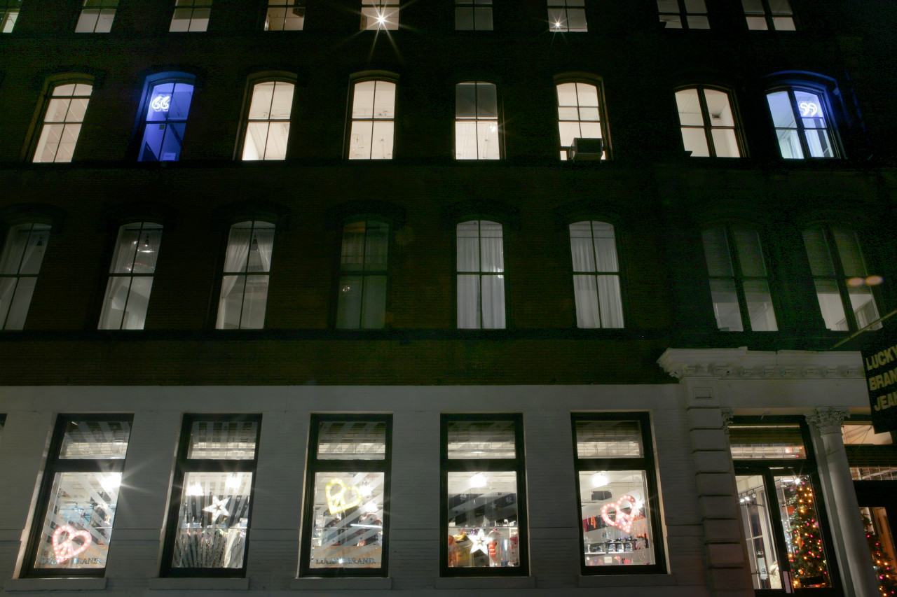 The exterior of a Soho building at night. Inside the third floor are two glowing blue neon quotation marks visible from outside.