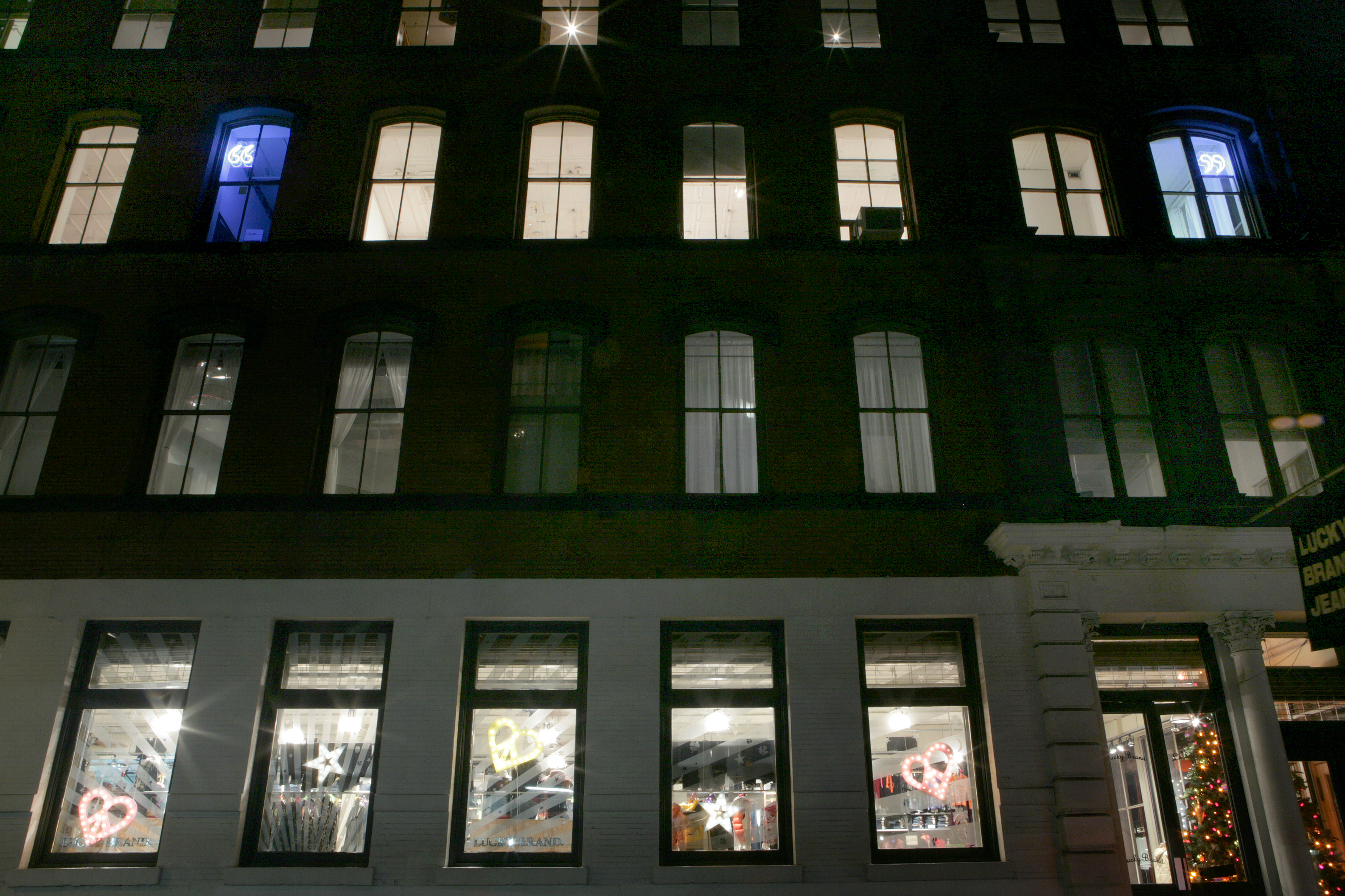 The exterior of a Soho building at night. Inside the third floor are two glowing blue neon quotation marks visible from outside.