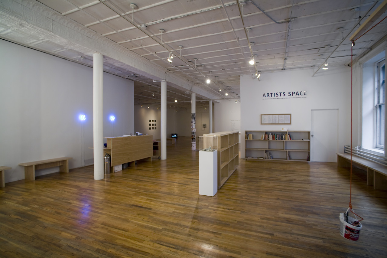 The interior of a Soho loft space. In the foreground, a plastic bucket hands from a red rope attached to an overhead pulley that is suspended from a wooden plank hanging overhead. 