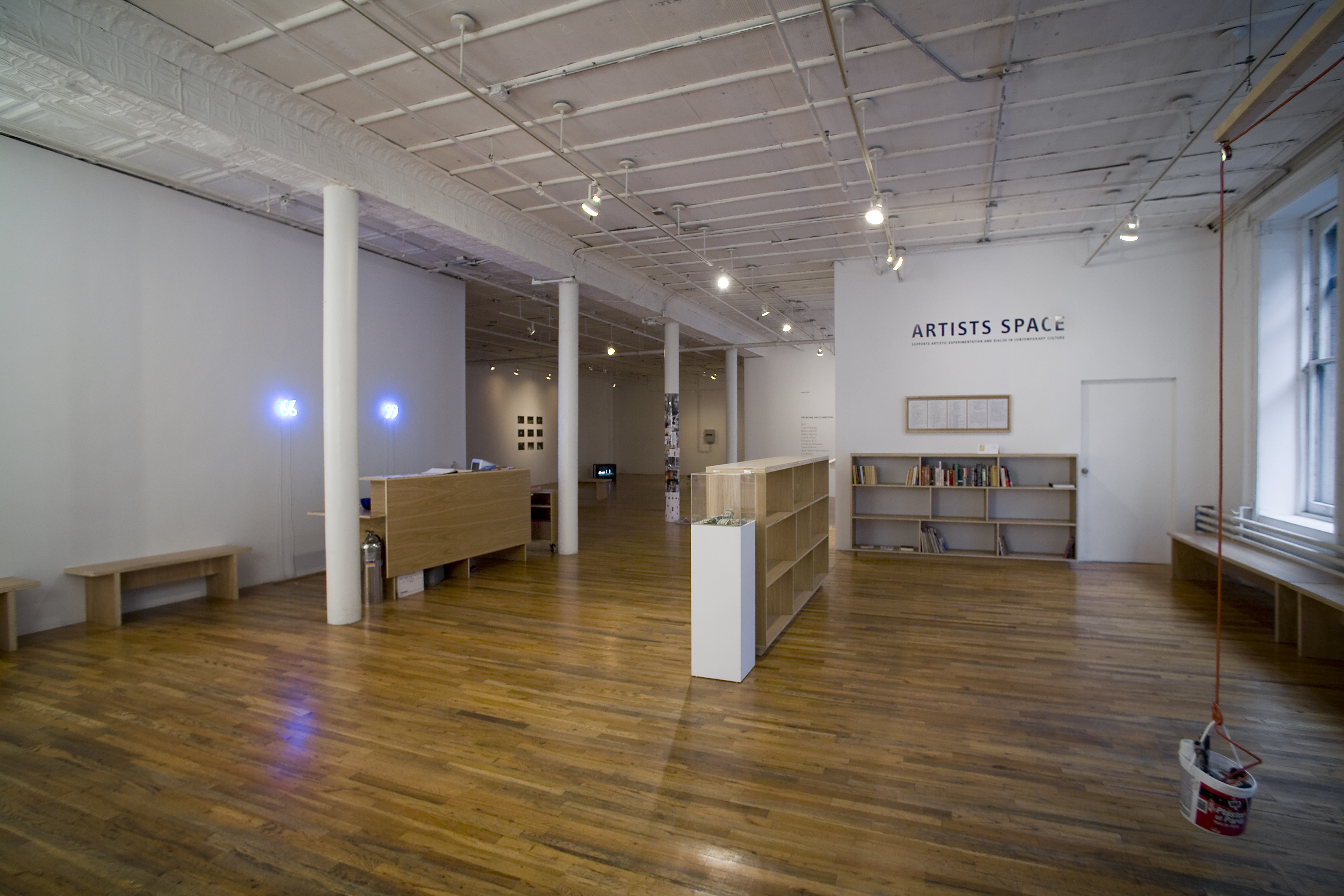 The interior of a Soho loft space. In the foreground, a plastic bucket hands from a red rope attached to an overhead pulley that is suspended from a wooden plank hanging overhead. '
