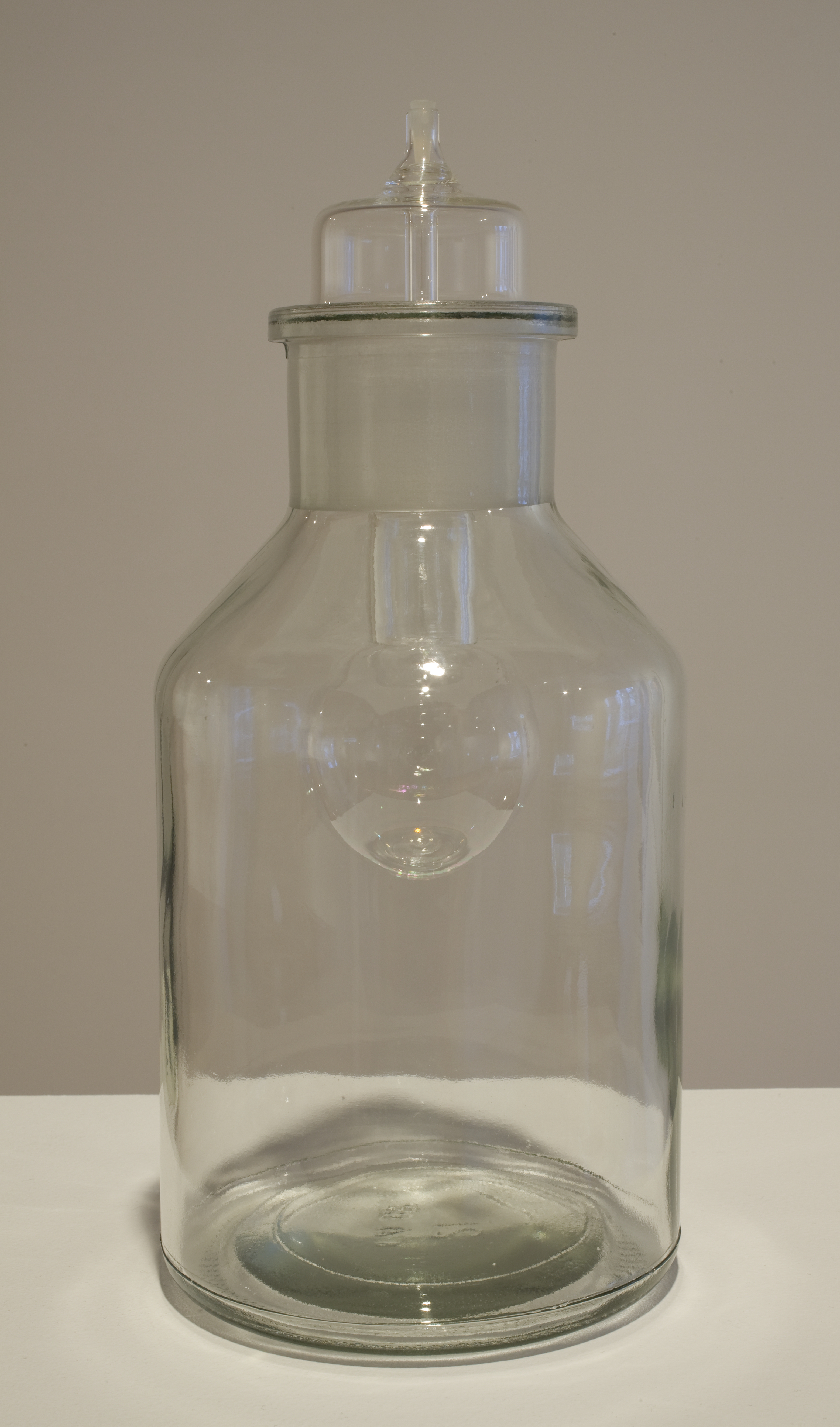 A wide cyclindrical glass bottle with a lightbulb inserted at its opening.