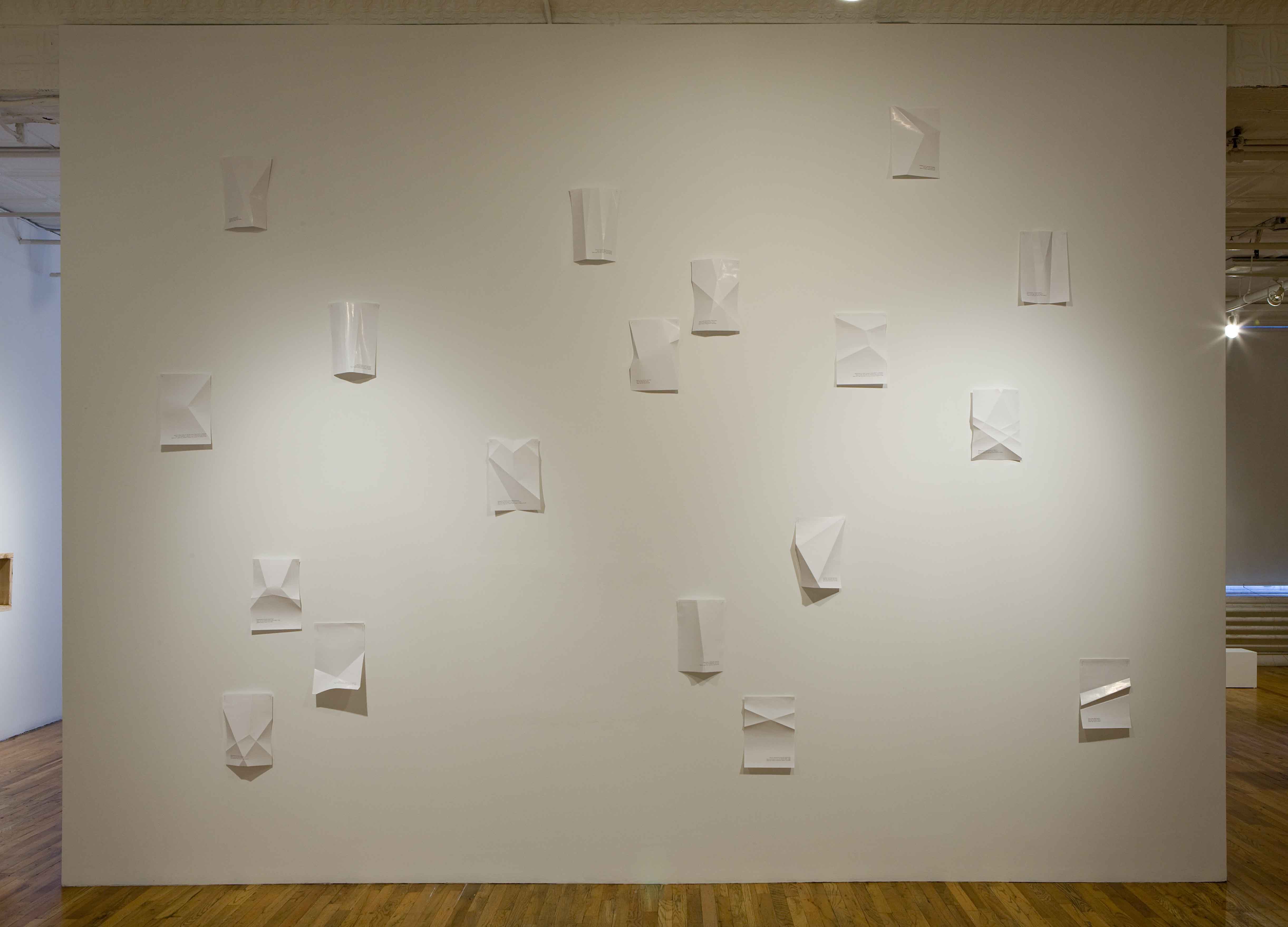 White glossy paper folded in geometric patterns against a white wall.