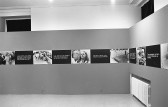 A continuous strip extends around the perimeter of the room, hung up on the walls. The strip alternates between photographic stills and black boxes overlaid with white text.