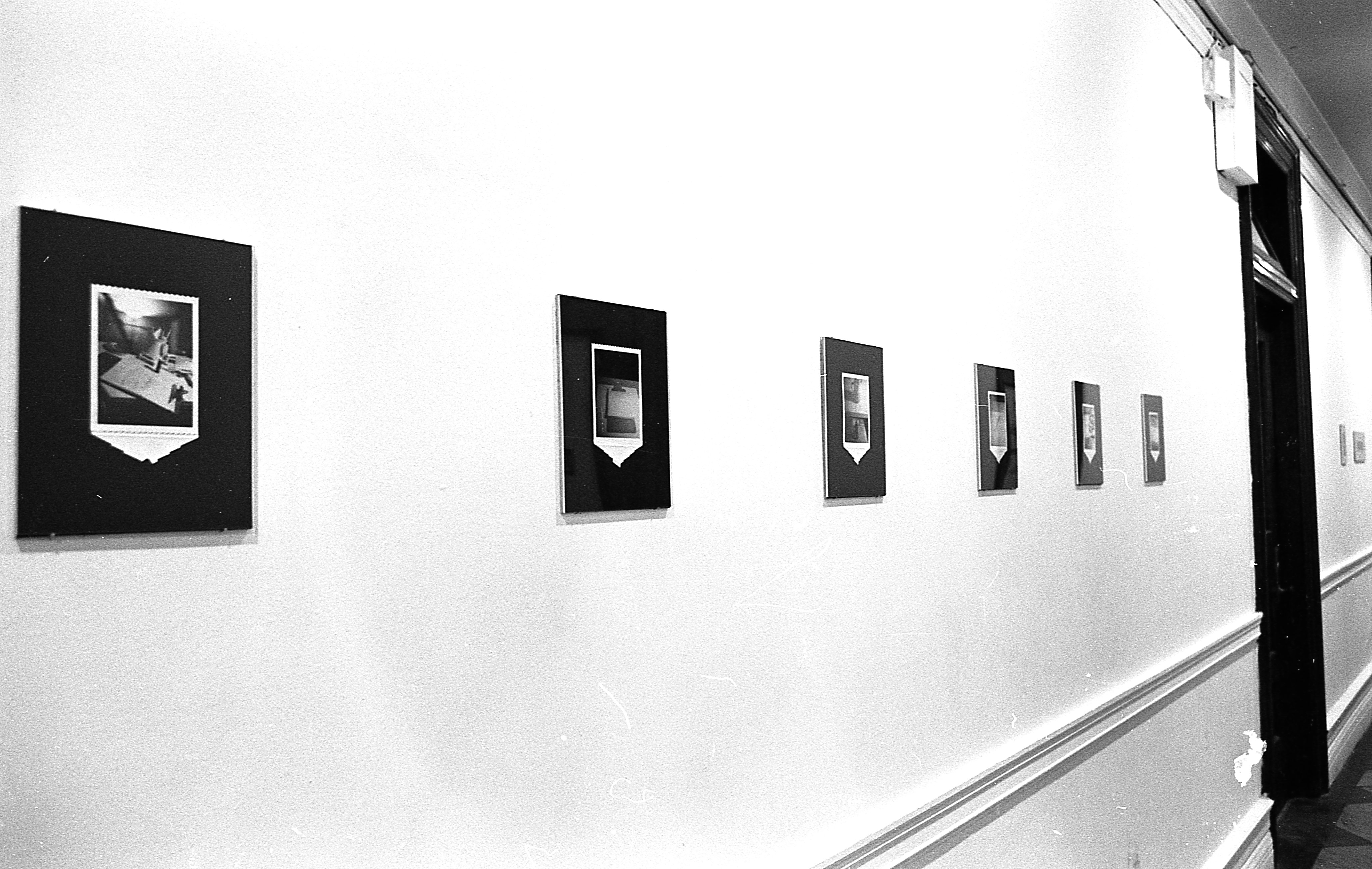Photographs mounted to black backgrounds are hung up in a row on a white wall.