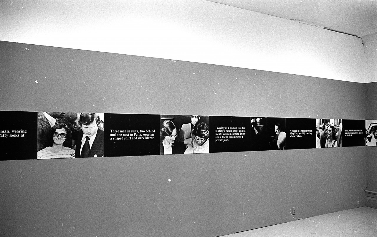 A continuous strip extends around the perimeter of the room, hung up on the walls. The strip alternates between photographic stills and black boxes overlaid with white text.