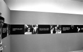 A continuous strip extends around the perimeter of the room, hung up on the walls. The strip alternates between photographic stills and black boxes overlaid with white text.