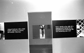 A continuous strip extends around the perimeter of the room, hung up on the walls. The strip alternates between photographic stills and black boxes overlaid with white text. In the center of the image is an open doorframe.