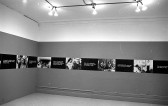A continuous strip extends around the perimeter of the room, hung up on the walls. The strip alternates between photographic stills and black boxes overlaid with white text.