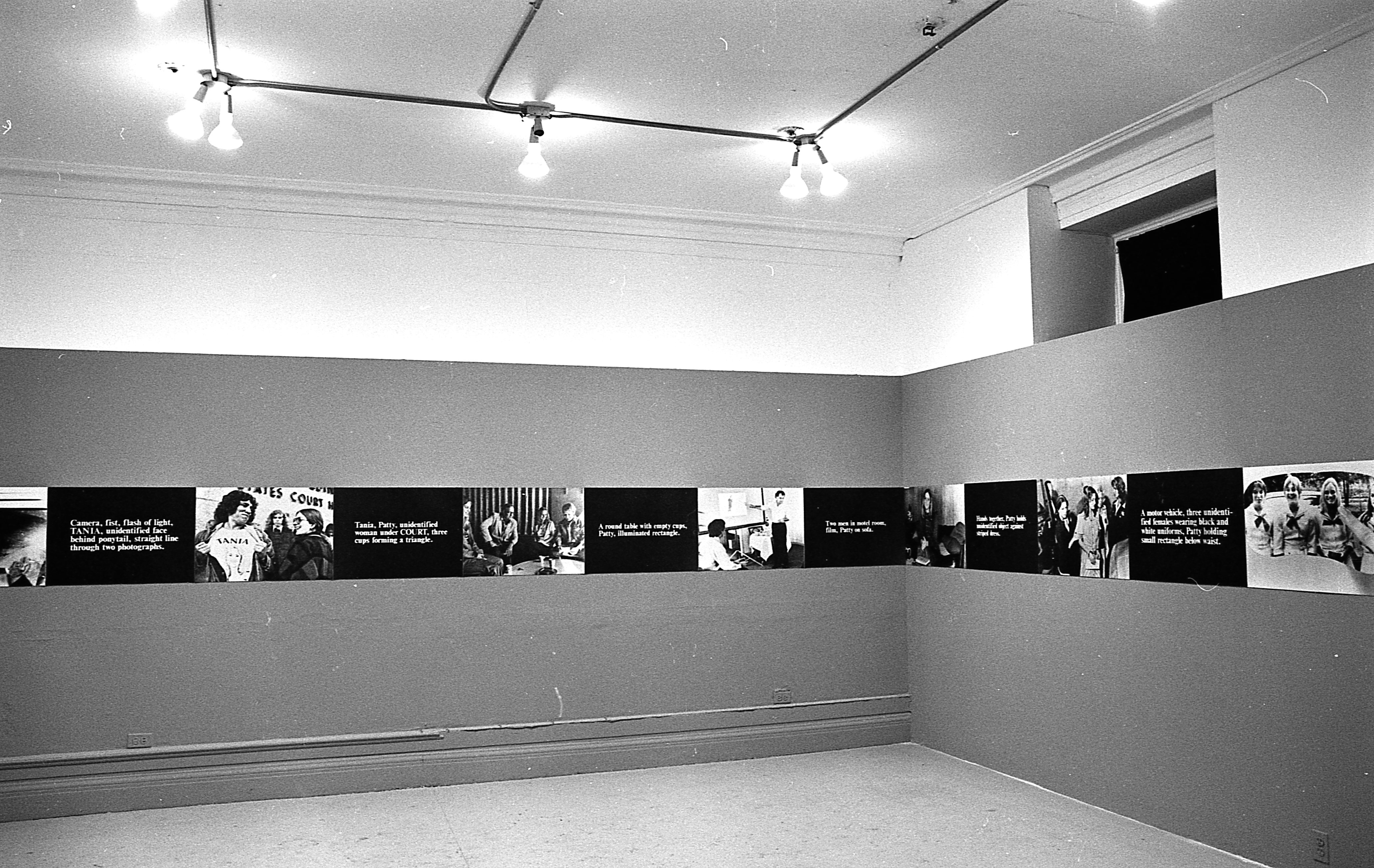A continuous strip extends around the perimeter of the room, hung up on the walls. The strip alternates between photographic stills and black boxes overlaid with white text.