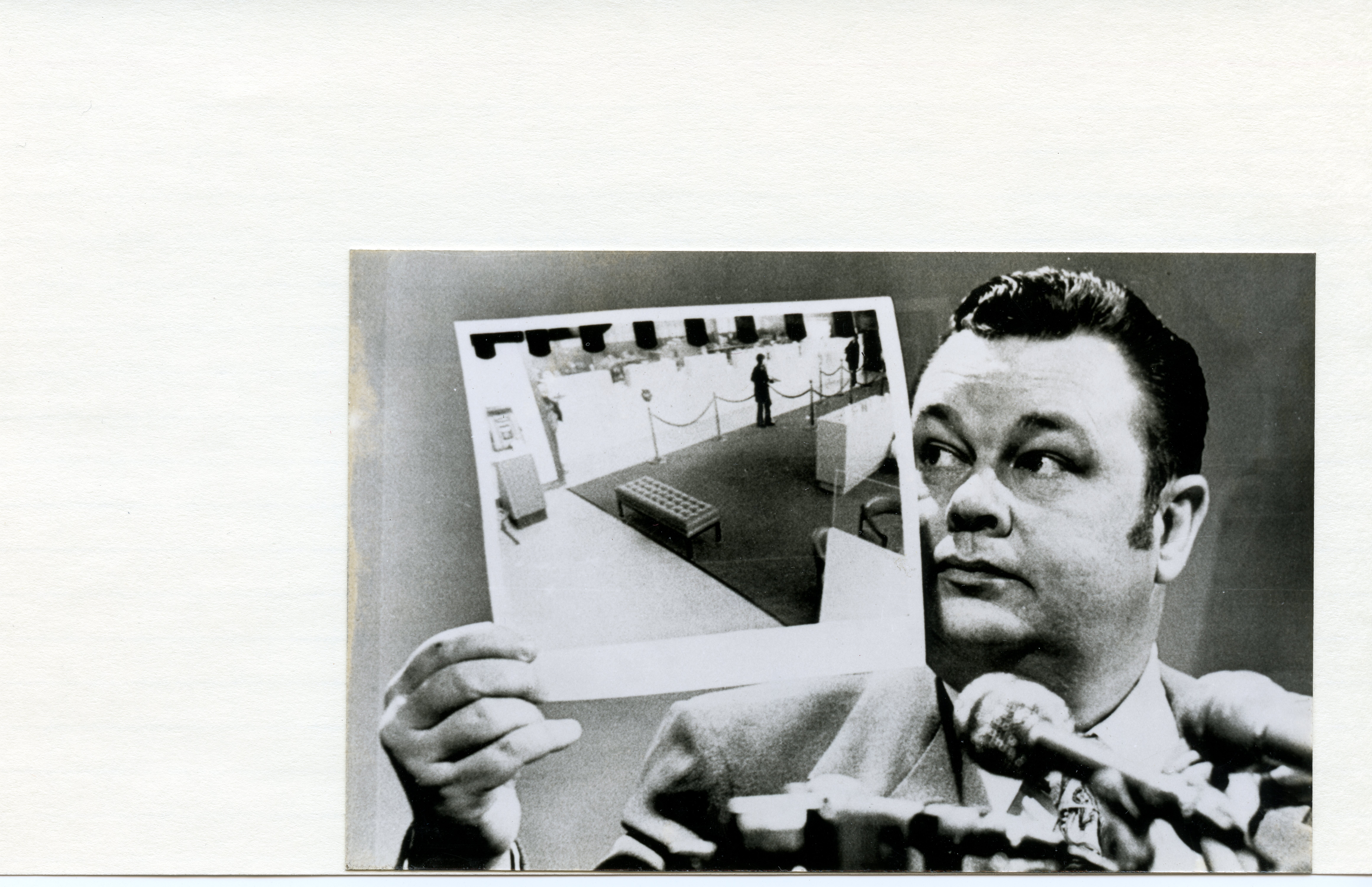 A man holds a photograph up to his face with a microphone directly in front of him.