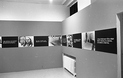 A continuous strip extends around the perimeter of the room, hung up on the walls. The strip alternates between photographic stills and black boxes overlaid with white text.